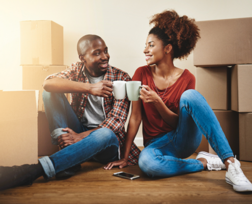 Couple sitting on the floor of their new home surrounded by moving boxes, celebrating together