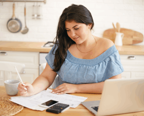 Self-employed woman reviewing bills and bank statements at home with laptop and calculator while preparing for a mortgage application