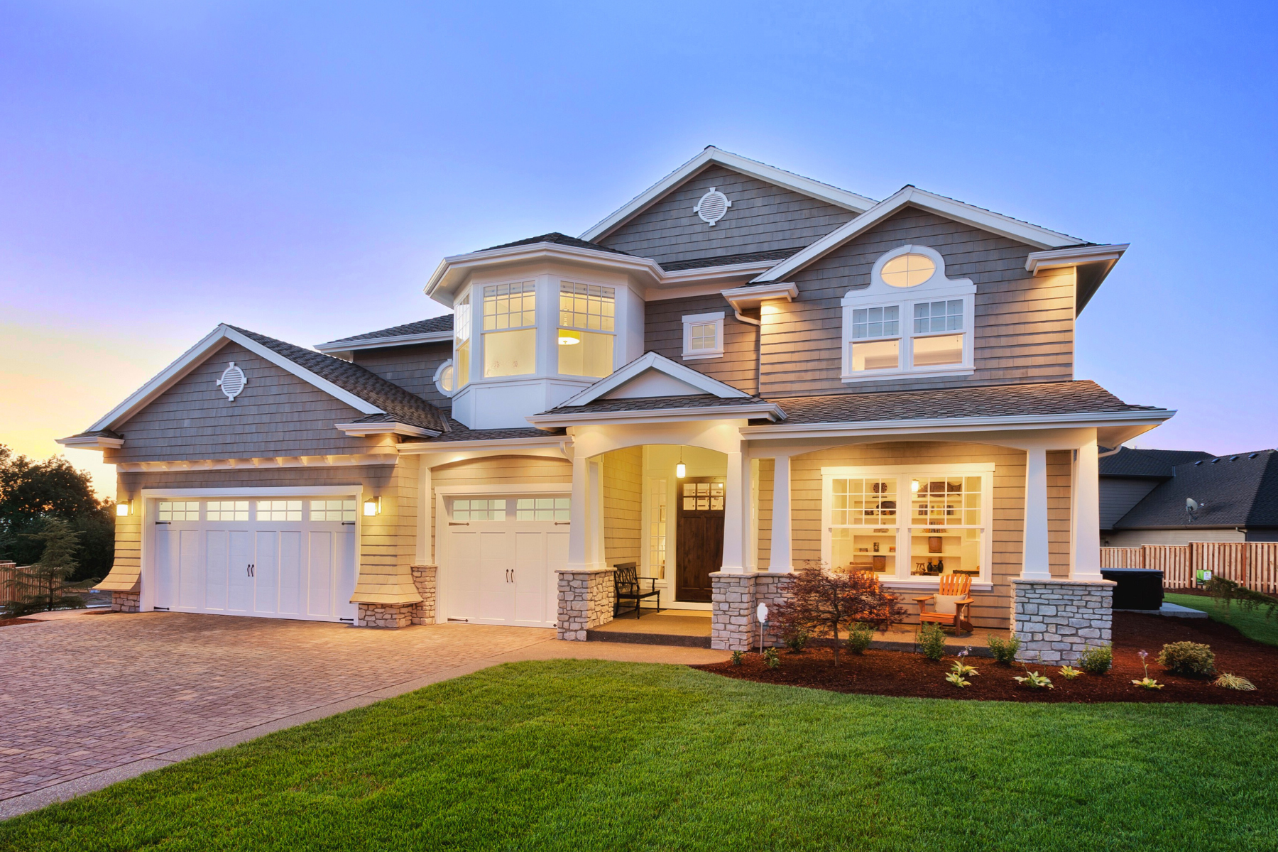 Modern two-story suburban home with warm exterior lighting at sunset, representing the dream of homeownership.